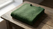 © Mathew - A folded green knitted woolen sweater resting on a rustic wooden table illuminated by soft window light