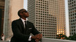 © ArtShop - Young black man in suit wearing sunglasses outdoors in city at sunset