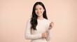 © Dilshan - Young Asian Woman Bright Smile Hands Raised White Sweater Peach Background Studio Portrait