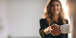 © Lady O - A smiling woman in a black blazer shaking hands with a business partner.