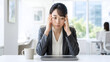 © M_Texture_Works JP - Japanese woman holding her head while sitting at home