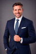 © Tom - Professional portrait of a confident smiling businessman wearing an elegant navy blue suit, white shirt and patterned tie against a neutral gray studio background. Polished corporate headshot represen