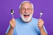 © NovaShots - Cheerful elderly grandfather holding cutlery and smiling on violet background.