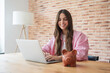 © Daniel - Young woman smiling at laptop while managing online banking and budgeting, piggy bank nearby symbolizing savings, investment planning and confident personal finance control