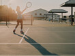 © visualstory - Young tennis player hitting a backhand shot on an outdoor tennis court at sunrise.