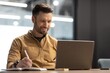 © Prostock-studio - Focused Caucasian Man In Mid 30s Writing Notes And Using Laptop At Desk In Modern Office, Engaged In Work Tasks, Professional Environment, Business Concept.