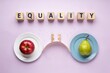 © Fahad - Equality concept with wooden blocks, red apple and green pear on balanced plates, social justice and fair distribution metaphor on purple background