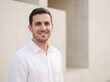 © Pixel Stock House - Portrait of handsome young man smiling in white casual shirt standing against clean modern concrete architectural wall, modern headshot of friendly attractive male professional outdoors daylight