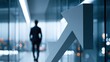 © KORANIS - A businessman walks down a modern office hallway as a large arrow graphic points upwards, symbolizing growth and success