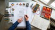 © Olena - Professional electrician reviewing an electrical wiring diagram with circuit breakers, cables and testing tools on a workbench. Modern electrical installation planning for residential and commercial p