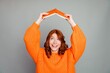 © deagreez - Smiling redhead woman in orange sweater holding a book overhead in a playful pose, cheerful student portrait expressing joy, creativity, learning and upbeat energy