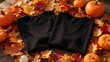 © Danish - Two blank black tshirts laying flat on a rustic wooden table surrounded by vibrant autumn maple leaves and several small decorative pumpkins for seasonal display