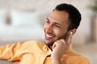 © Prostock-studio - Smiling African American Man In His 20s Or 30s With Earbuds Enjoying Music Or Podcast While Relaxing At Home. Casual Lifestyle Setting Representing Modern Home Environment And Enjoyment.