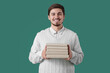 © Pixel-Shot - Young man with stack of books on green background