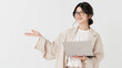 © pattozher - Elegant Presentation: A professional woman with glasses and a stylish beige blazer confidently holds a laptop, extending her hand to gesture towards an unseen point.