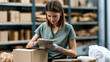 © Katerina - Female returns specialist using tablet to process customer return beside cardboard box in warehouse