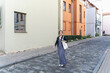 © Tatiana Kolosovskaya - Woman 40s in striped dress walking narrow cobblestone street with tote bag, colorful buildings