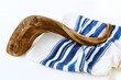 © Audrey - The Jewish shofar horn is positioned on the white tallit prayer shawl. Traditional ceremonial items for Rosh Hashanah and Yom Kippur observances. Religious accessories displayed against a white backdr