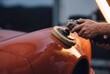 © AdPremium - Professional auto detailer polishing orange car body using electric rotary buffing machine in workshop