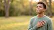© Kaluya Stock - Grateful young man holding hand on chest and smiling outdoors in park