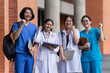 © Prot - Asian healthcare students celebrate together outside a university building, raising their fists with smiles while carrying study materials and technology during an energetic campus moment.