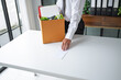 © Charlie's - Businessman Sending Resignation Letter to Boss While Holding Cardboard Box Beside Office Desk After Career Change or Job Loss.