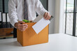 © Charlie's - Businessman Sending Resignation Letter to Boss While Holding Cardboard Box Beside Office Desk After Career Change or Job Loss.