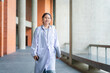 © iPoguz - Young doctor or intern wearing stethoscope walking in university corridor, smiling female medical student in white lab coat holding laptop and smartphone walking at university campus
