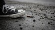 © Green - Gritty street scene featuring a discarded cigarette butt lying on a wet, cracked urban pavement next to a casual canvas shoe, depicting pollution and urban neglect