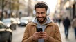 © Panpatsa - Man wearing headphones smiles while using his smartphone amidst blurred city background cars.