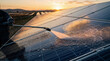 © CK Studio - Solar panels being cleaned by worker with pressure washer at sunset in large solar farm, representing sustainable energy maintenance.