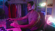 © Krakenimages.com - Young man wearing headset plays on keyboard and mouse, hand on keys, seated in studio with neon gamepad sign and shelves; focused gaming session.