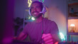 © Krakenimages.com - Man wearing headset pumps fists and presses keys with hands near keyboard under neon lights in streaming studio; excitement focus.