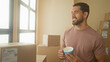 © Krakenimages.com - Man holding a blue mug and smiling, standing among stacked shipping boxes and parcels while packing in a building; contentment entrepreneurship.