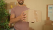 © Krakenimages.com - Man offers cardboard parcel with outstretched hand in a small business packing area inside a building; friendly service.