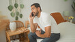 © Krakenimages.com - Man sits on bed holding smartphone to ear, smiling broadly and gesturing with right hand in a bedroom; cozy conversation happiness.