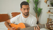 © Krakenimages.com - Man playing nylon string acoustic guitar, fingers fretting chords while seated on a bed in a bedroom; quiet practice serenity.