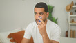 © Krakenimages.com - Young hispanic man holding blue creditcard to his nose while sitting on a bed in a building bedroom, inspecting and smelling the card; contemplation.