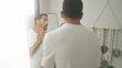 © Krakenimages.com - Young man touching face in mirror while applying skincare to his cheeks in a bright dressing area inside a building; confidence calm.