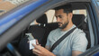 © Krakenimages.com - Man holds smartphone and receipt with both hands, seatbelt fastened, reading intently inside parked car on street; focused concentration.