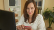 © Krakenimages.com - Woman tapping smartphone with fingers at desk in a studio with computer, mug and paperwork visible; concentration productivity.