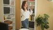 © Krakenimages.com - Woman holds smartphone to ear, hand raised palm up, white blouse and jeans, standing by bookshelf and lamp in a building office; concern remote work conversation.