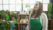 © Krakenimages.com - Woman florist in green apron closes eyes and inhales the scent of a potted monstera plant in a studio; serenity.
