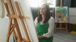 © Krakenimages.com - Woman in green apron studies a large canvas on an easel with hand to chin and folded arms while gazing at paint marks in a studio; contemplation.