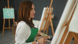 © Krakenimages.com - Woman painter in apron holds paintbrush to chin and studies canvas at easel in art studio, palette visible; contemplation focus.