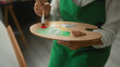 © Krakenimages.com - Woman middle age artist wearing green apron holding palette and paintbrush, hand mixing paint, paints canvas in studio; creative concentration.