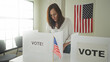 © Krakenimages.com - Woman places ballot into a white voting booth at a polling table in building with american flag and privacy screen visible; civic duty pride.