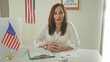 © Krakenimages.com - Woman in white blouse folds hands over ballot envelope and clipboard on table inside civic building with small american flag and vote poster; responsibility democracy.