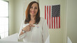 © Krakenimages.com - Woman points finger to i voted sticker at polling station inside voting booth with american flag visible; pride civic duty.