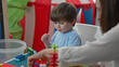 © Krakenimages.com - Boy plays with colorful building blocks while woman teacher guides with hands on the table in a preschool classroom; focused learning.